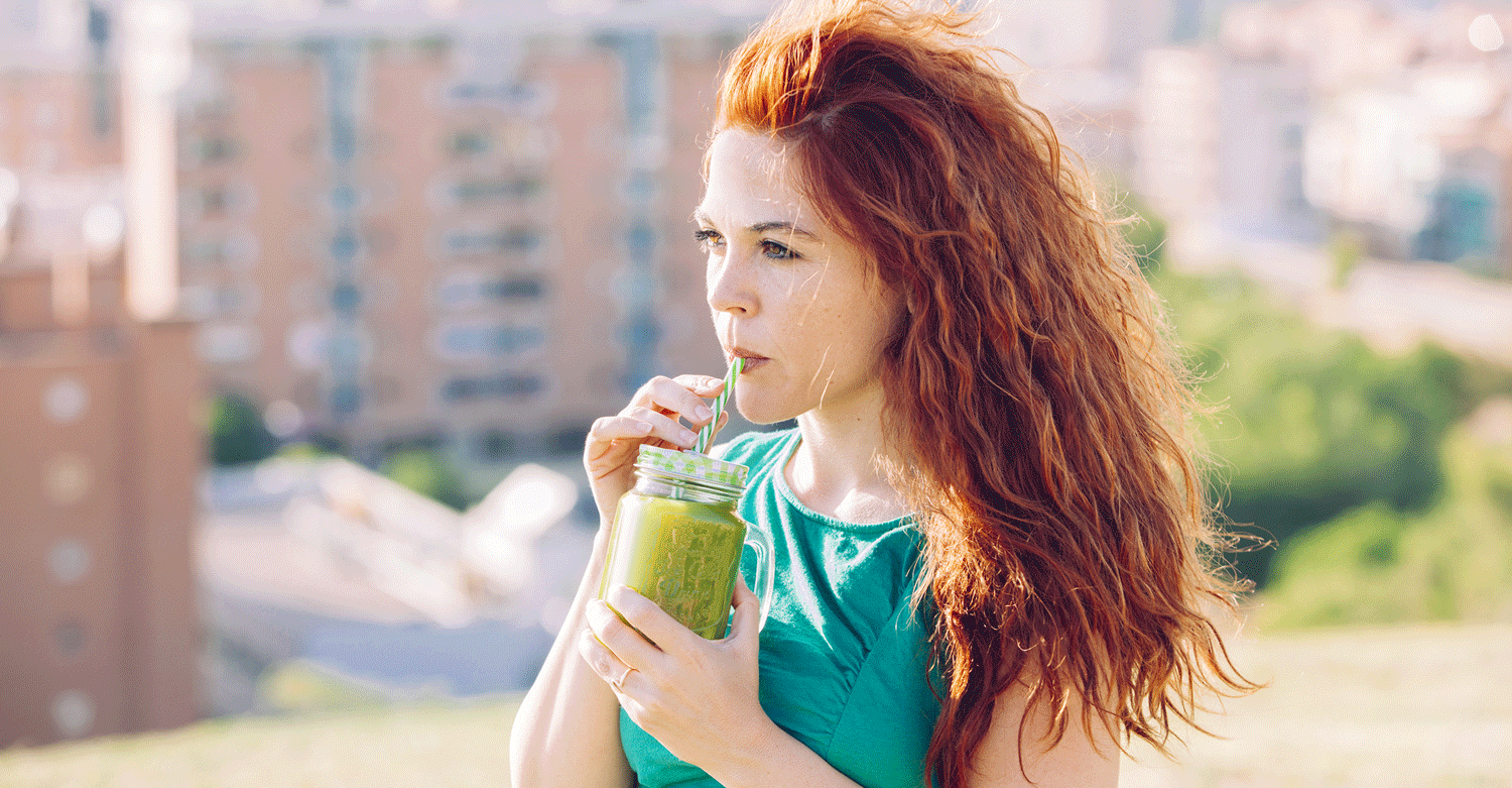 Junge rothaarige Frau trinken einen Smoothie aus einem Glas mit Strohhalm