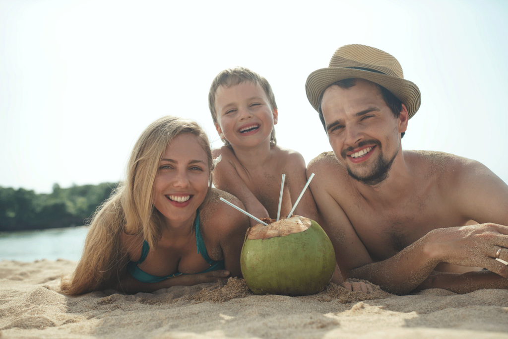 Familie liegt am Strand und trinkt aus einer Kokosnnuss